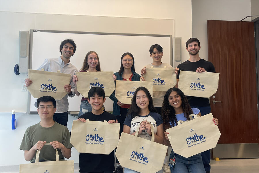 Student volunteer with SOOTHE hold up canvas tote bags in a group photo