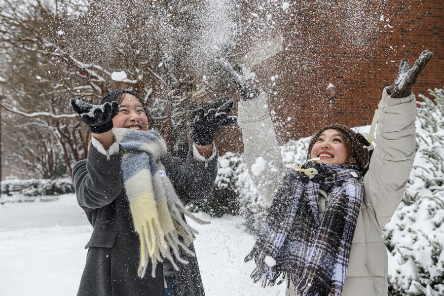 Two students throw snow in the air and smile