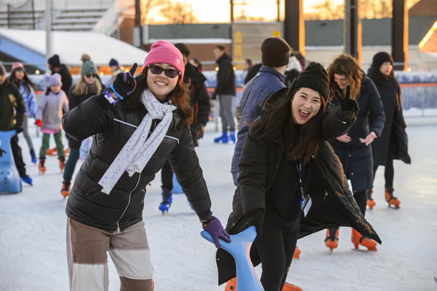 Two ice skaters smile to the camera, making peace signs.