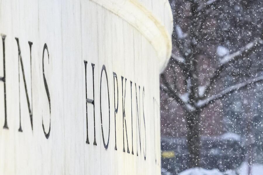 Snow falls next to a large marble sign that reads 