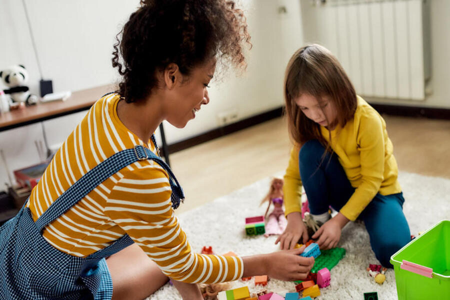 Child and a care giver sitting on the floor with building blocks