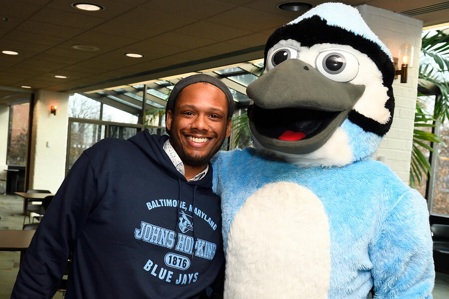 A man in a JHU sweatshirt poses with Jay, the university mascot