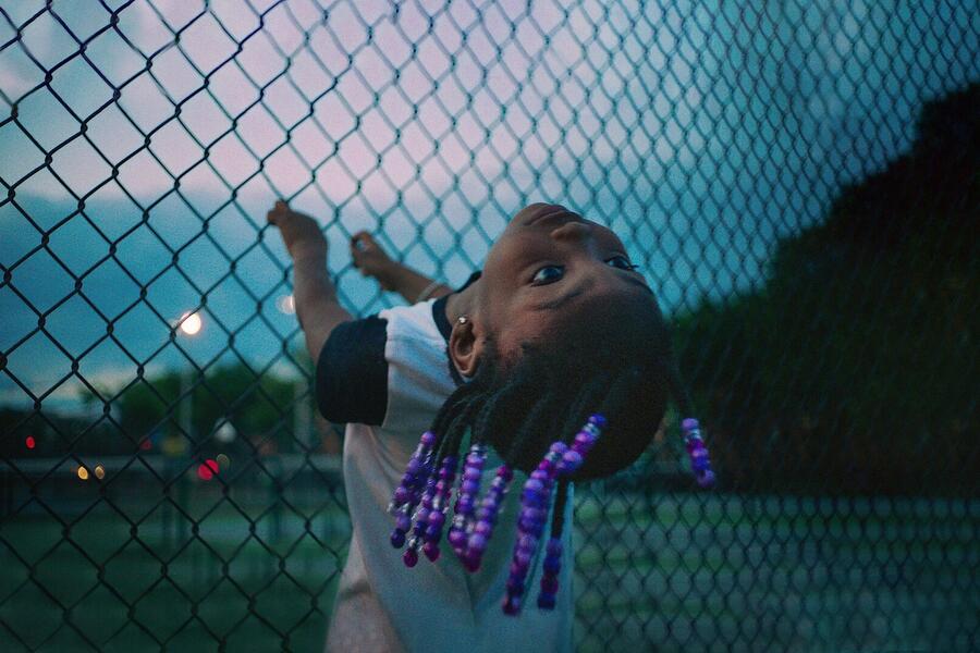 A young girl bends backwards while clinging to a chain-link fence