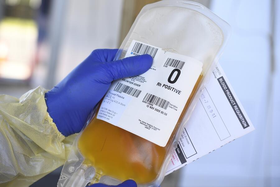 A gloved hand holds up a bag of plasma.