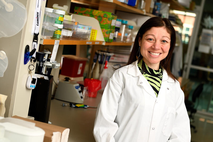 A woman in a white lab coat poses for a photo in a lab setting