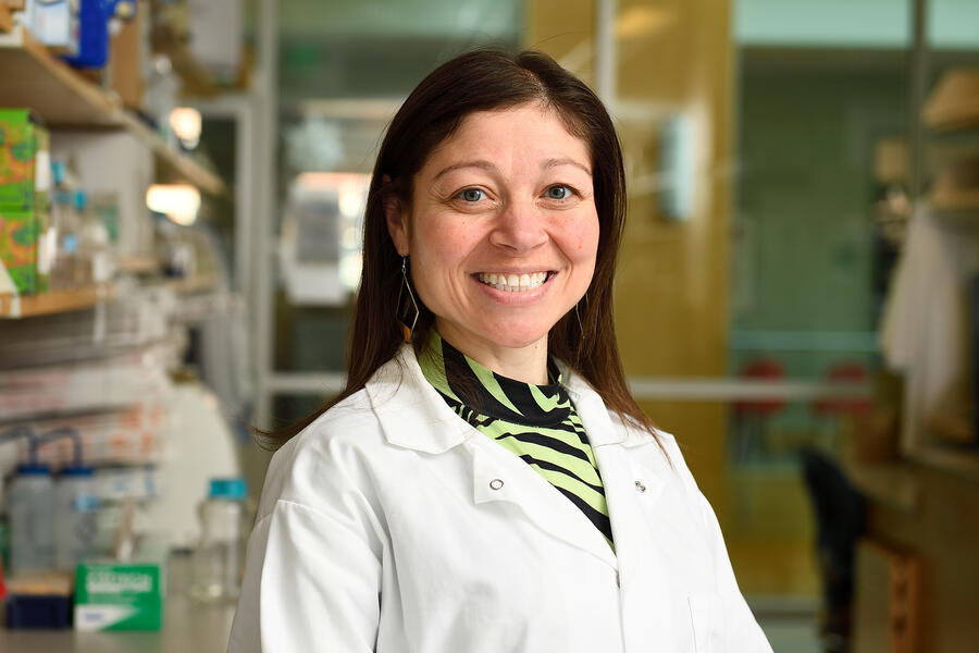 A woman in a white lab coat poses for a photo in a lab setting