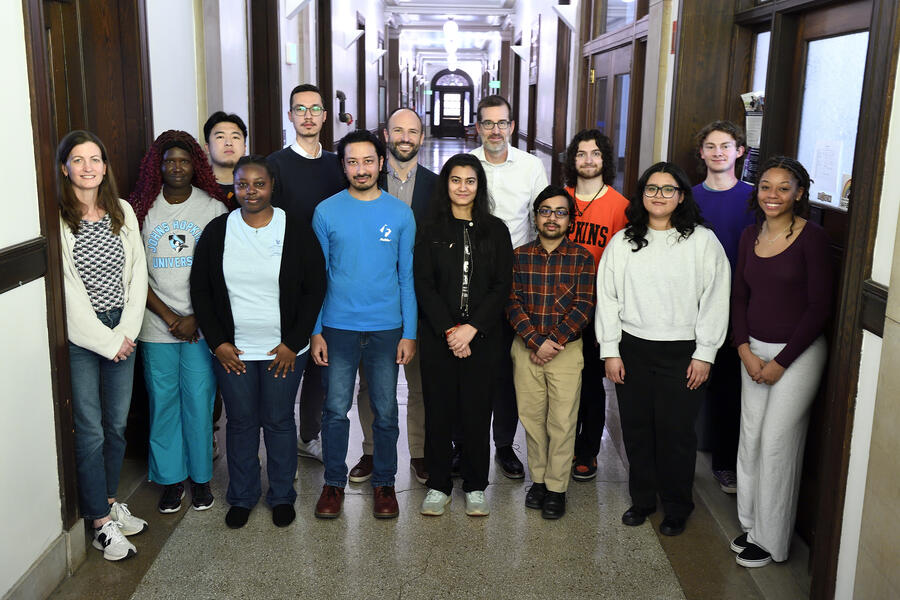 14 people pose for a group photo while standing in a hallway.