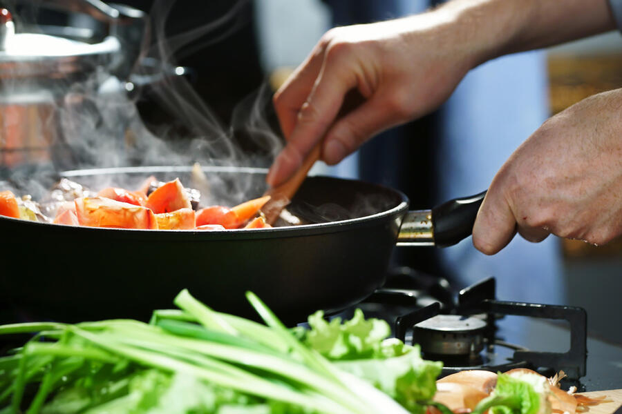 A man prepares vegetables in a skillet in his home kitchen