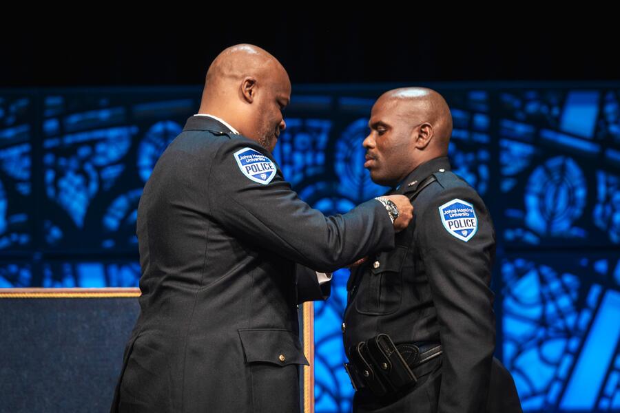 Branville Bard pins a badge onto Officer John Marcus during a police academy graduation ceremony.