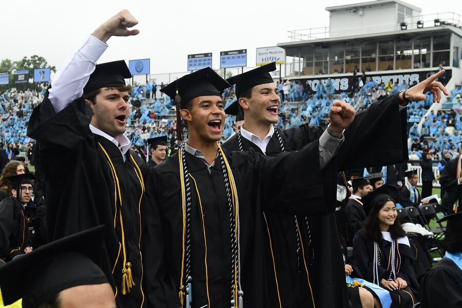 Three graduating students stand and cheer at JHU Commencement 2025.