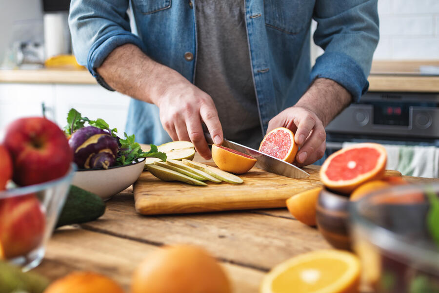 Closeup of a man holding a knife cutting slices of fruit.