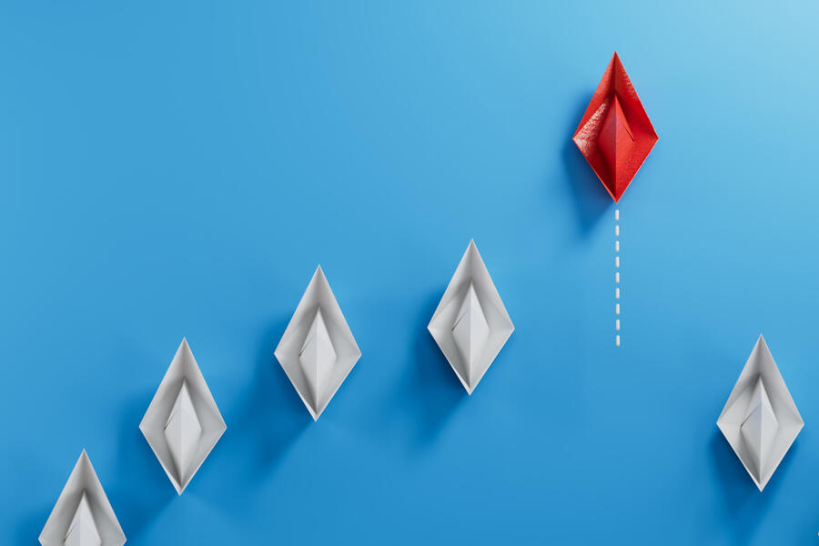 A red paper boat leads white paper boats behind it