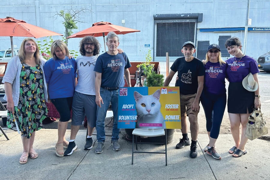 Seven volunteers stand in a row next to a sign reading "ADOPT. FOSTER. VOLUNTEER. DONATE." 