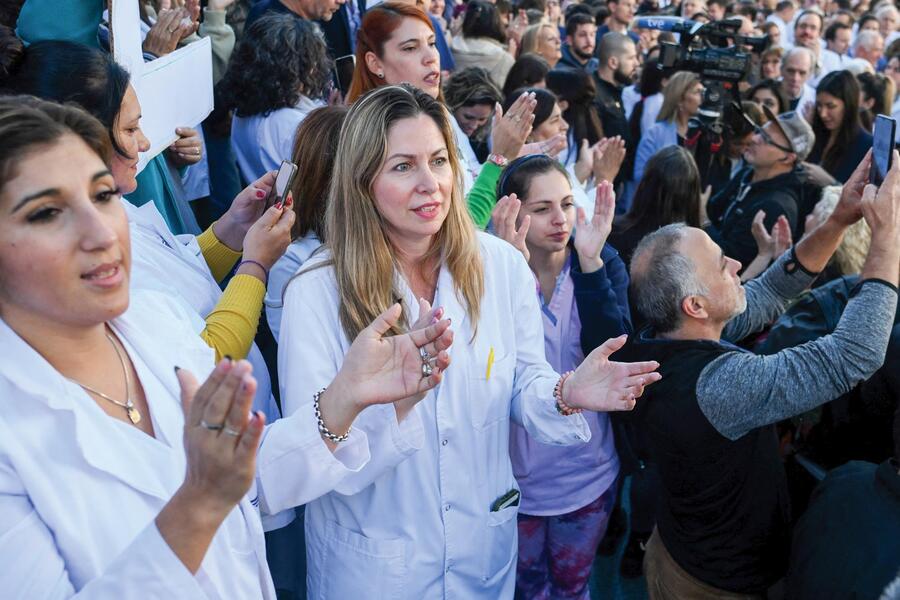 Two women in white lab coats are pictured among a large protest crowd