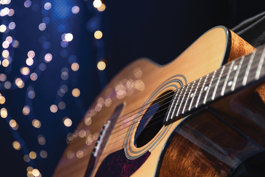 An acoustic guitar on a dark blue background with white twinkle lights