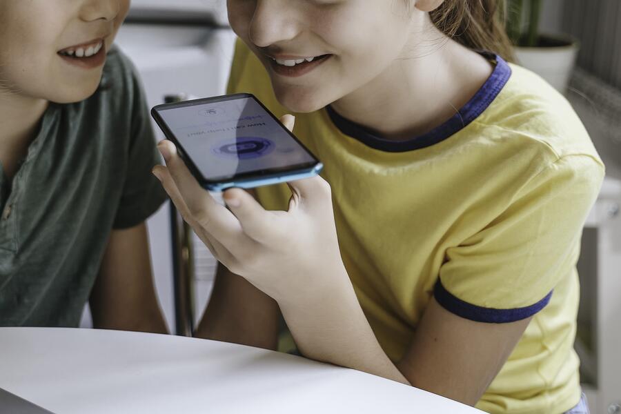 Two children speak to a chatbot on a cellphone.