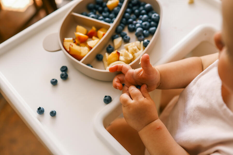 Photography of a toddler, slightly out of focus, eating from a plate of blueberries and peach slices