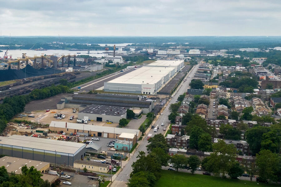 An aerial view of a coal terminal at left, including large piles of coal and rail cars, and a nearby neighborhood at right