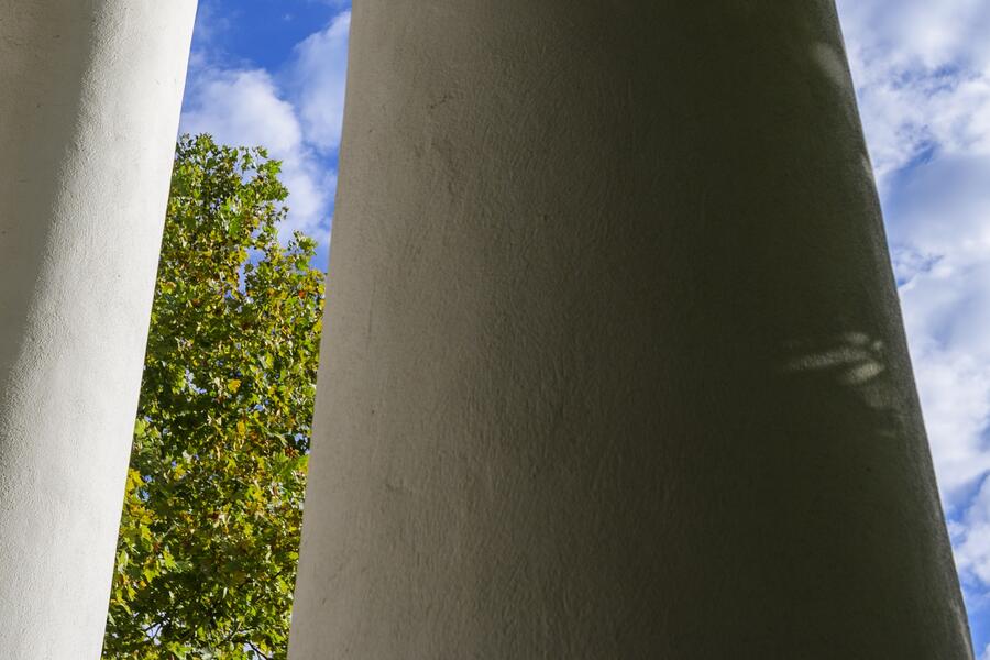 Columns stand tall in front of green trees and a bright blue sky with white clouds.