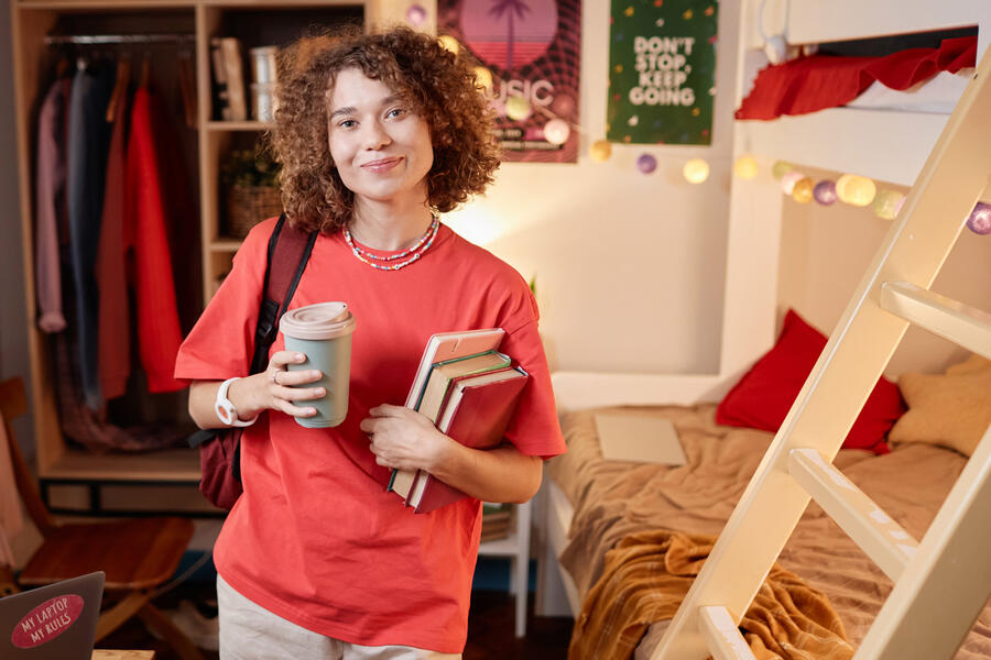 College student holding books in her dorm room.