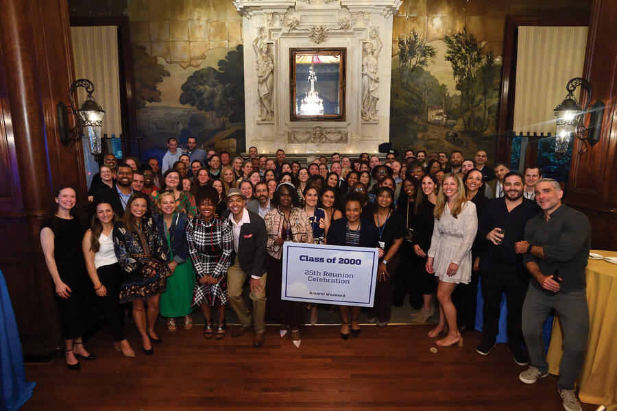 A large group of alumni pose behind a banner that says "Class of 2000, 25th Reunion Celebration"