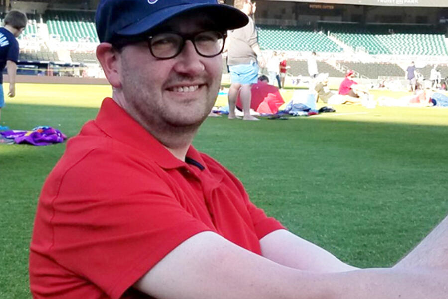 A man in a red shirt and Atlanta Braves hat sits on the baseball field at Atlanta's Truist Park