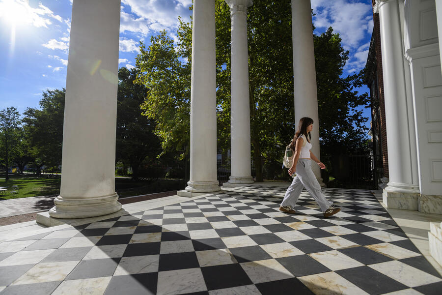 A student walks across the black and white tiled porch outside Gilman Hall