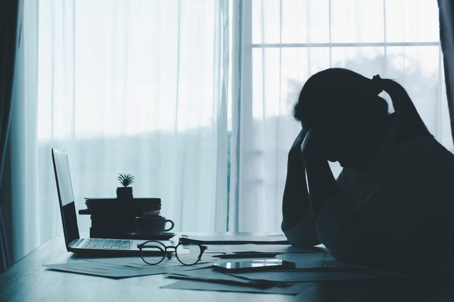 silhouette of a woman sitting at a desk with an open laptop and her head in her hands