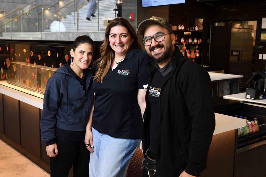 Three Koshary Corner staff smile for a picture in front of their food stall in the Bloomberg Student Center.
