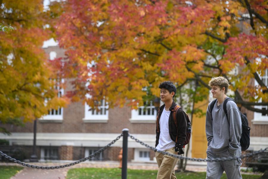 Students walk along the brick paths of the Homewood campus with fall foliage in the background