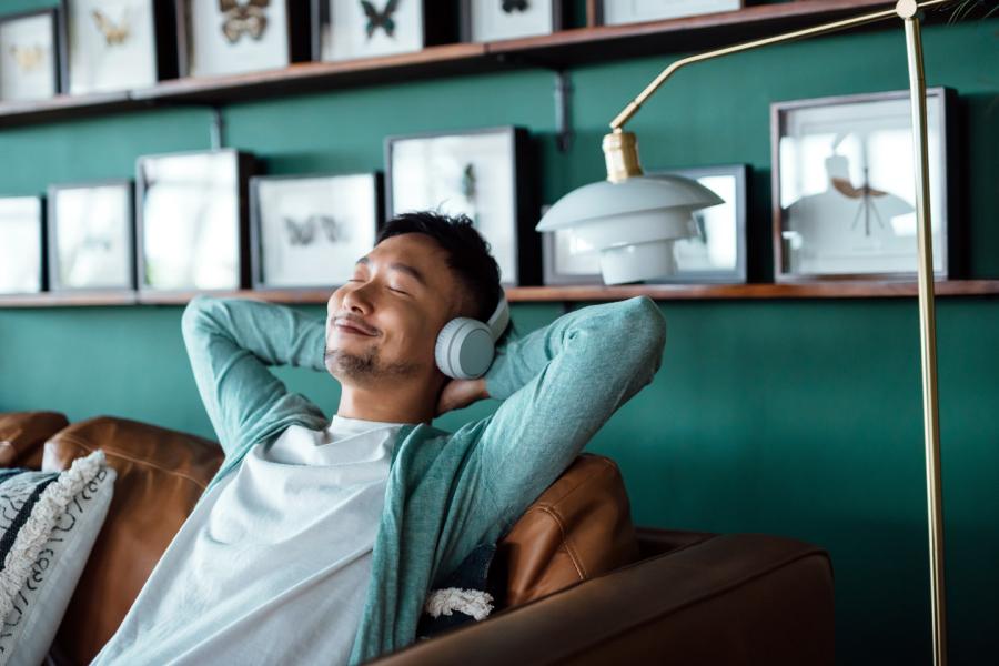 Young man wearing headphones leans back peacefully with his hands clasped behind his head.