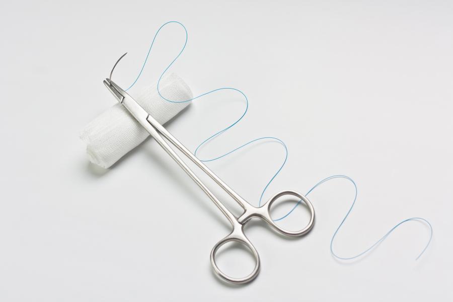 Needle holder put on white bandage as suture set