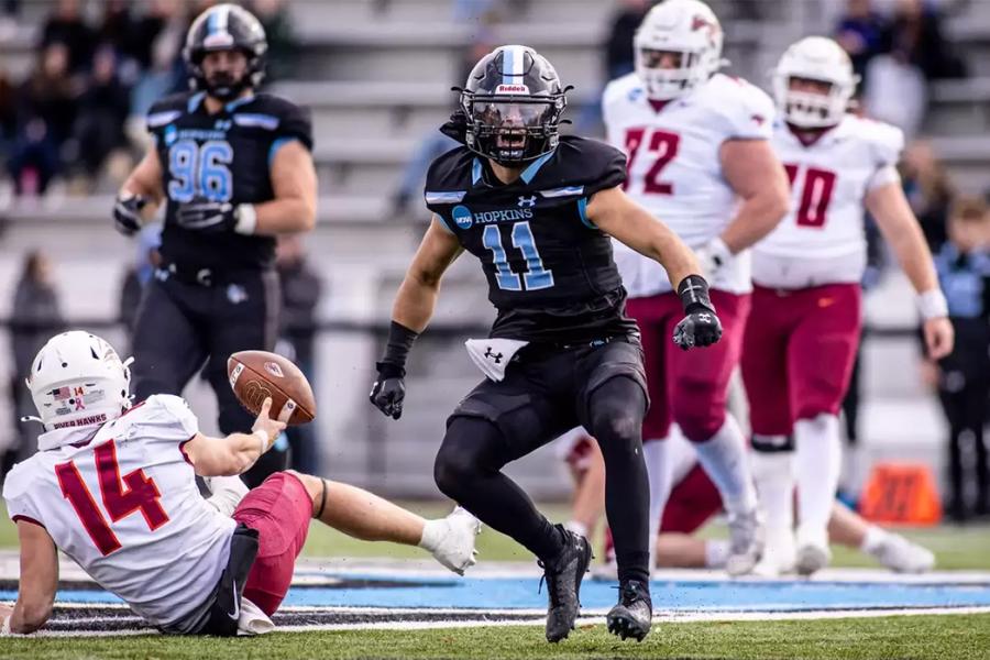 A football player in a black jersey celebrates after making a tackle
