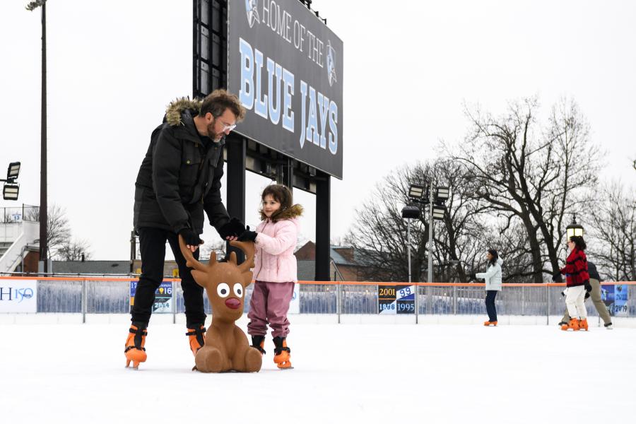 A parent and preschooler skate on an outdoor ice rink.