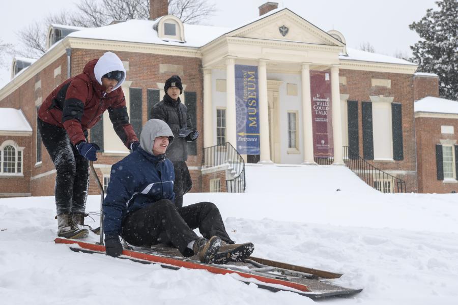 A group of college students get ready to send one of their own down a snowy hill on a sled.