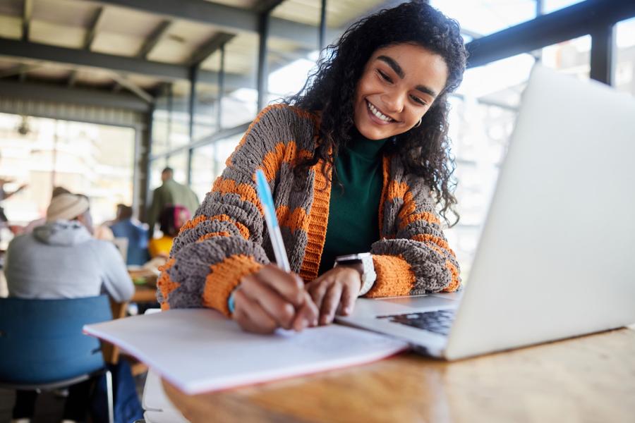 College student writing on a notepad next to her laptop.