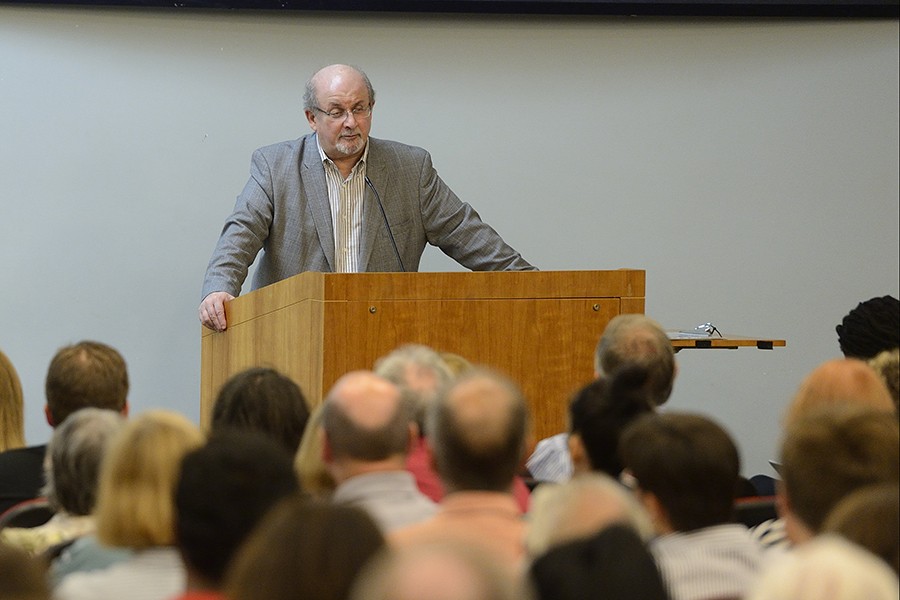 Salman Rushdie grips both sides of a wooden podium as he addresses a crowd