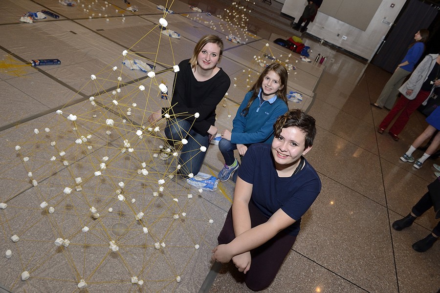 Three middle schoolers kneel beside their spaghetti structure which resembles a geodesic dome