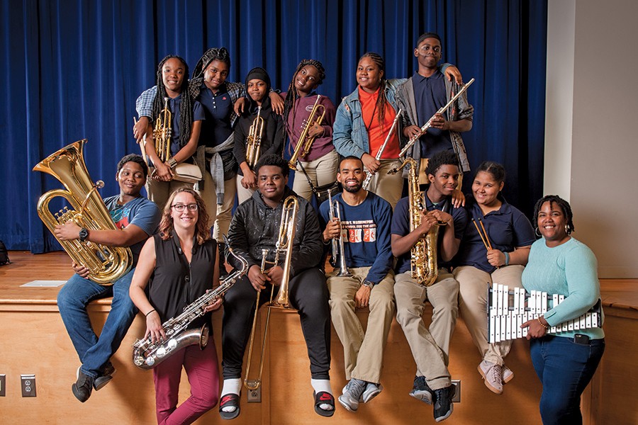 A group of people and students pose with their instruments on the edge of the stage