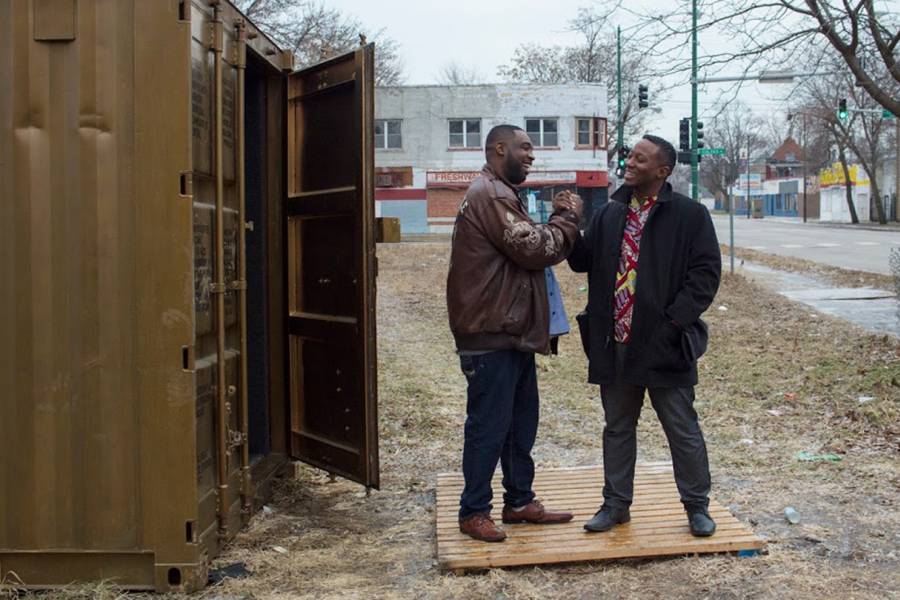 Two men shake hands outside of a gold shipping container in Chicago
