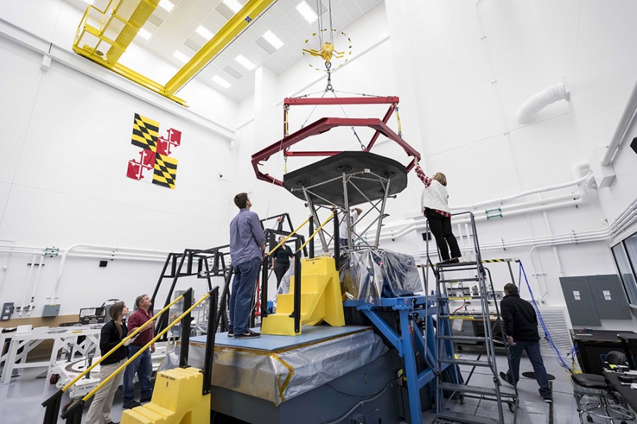 In a giant lab room featuring the Maryland flag on a wall, a team inspects the heat shield and prepares to box it for shipping