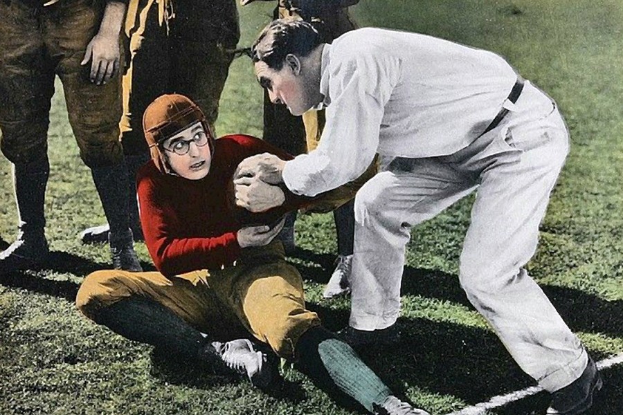 A colorized photo shows a man in a leather football helmet struggling with a referee to hold onto the ball