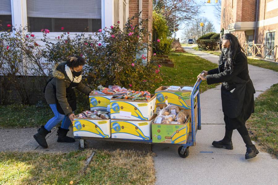 Volunteers push a cart laden with perishable food items including bread and carrots