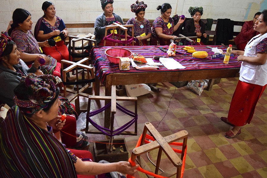 Women wearing traditional headdresses and clothing learn a basketweaving technique