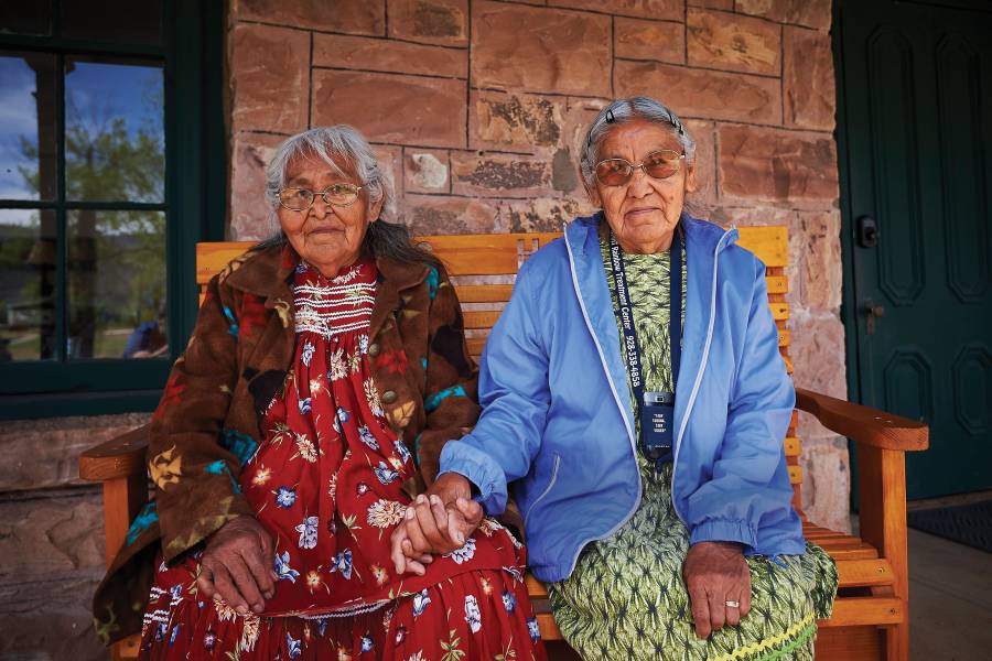 White Mountain Apache elders hold hands while sitting on a bench