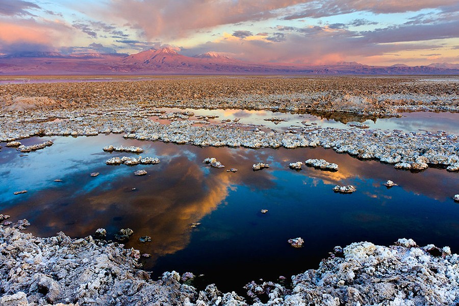 Large salt flat with cloud reflected in blue water and pink mountains on the horizon