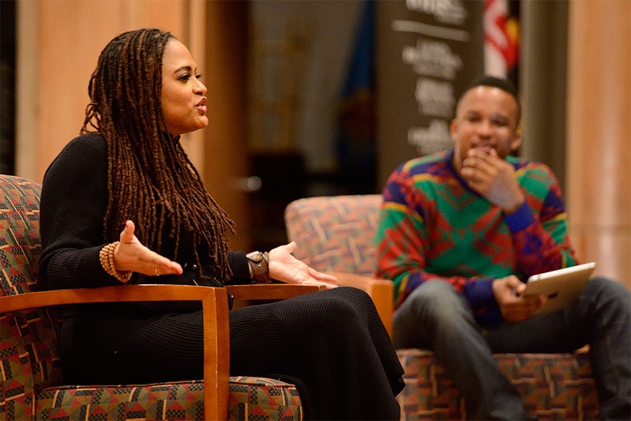 Ava DuVernay sits in a chair on stage