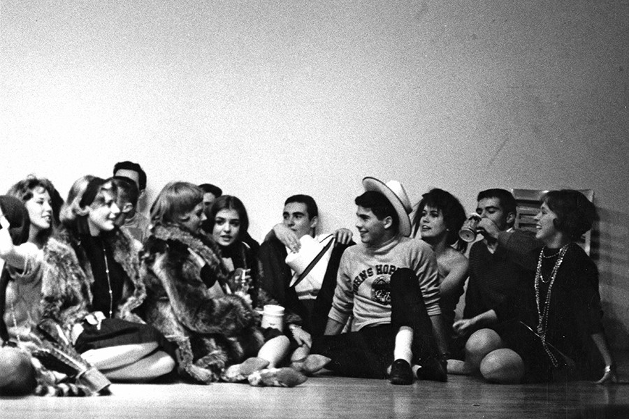 A grainy black and white photo shows male and female students sitting on a floor together