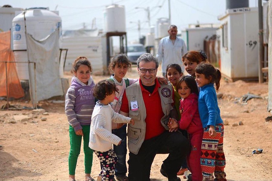 A man kneels beside a group of children in a Syrian refugee settlement