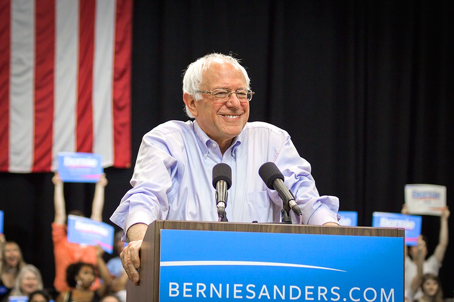 Bernie Sanders smiles at podium with US. flag backdrop